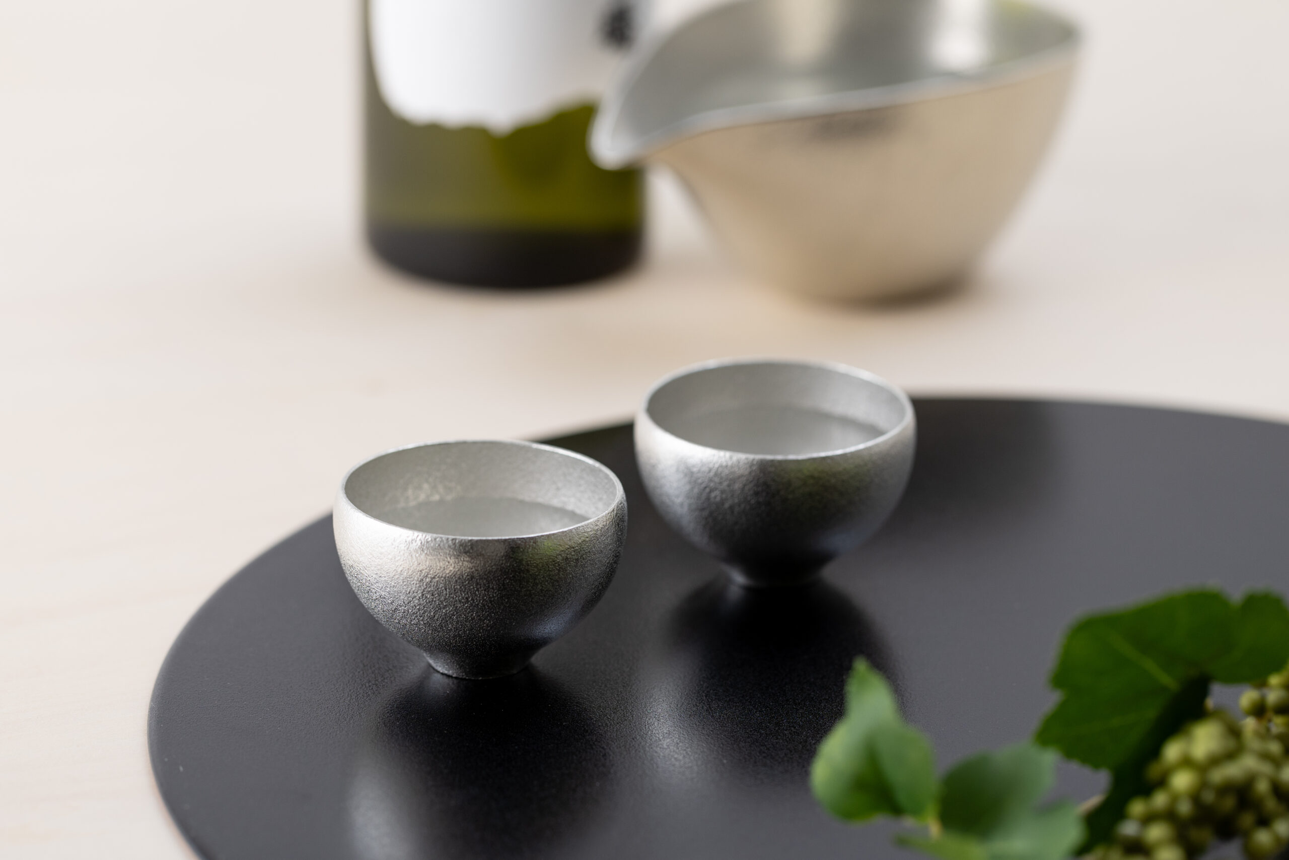 Nousaku tin sake cups on a dark tray with sake bottle